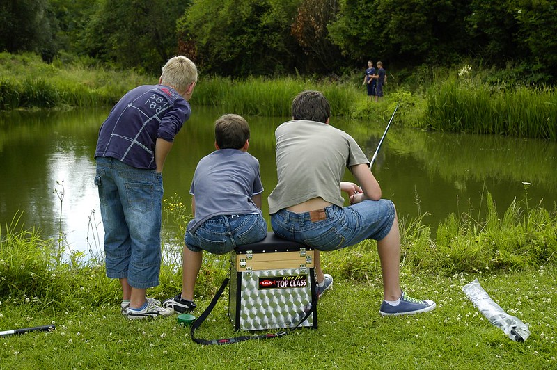 Trois enfants assis à coté de l'étang de pêche qui regard attentivement la surface de l'eau.